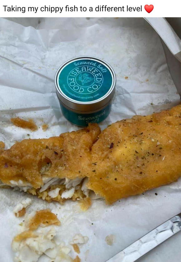 Image from a Facebook post showing chip shop battered cod on chip paper with seaweed salt sprinkled on top and a tin of seaweed salt next to it - title says 'taking my chippy fish to a different level' with a red heart