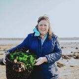 Naomi holding a basket of cut seaweed with beach in the background 