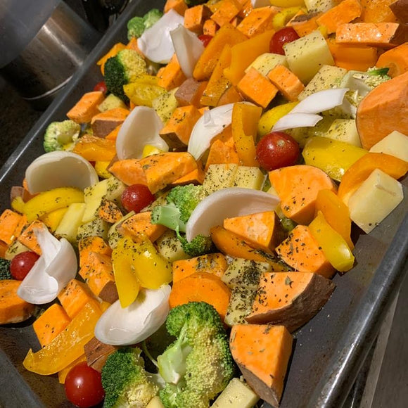 Chopped vegetables including sweet potato, onion, pepper, cherry tomatoes and broccoli on a baking tray ready for the oven - sprinkled with herby seaweed seasoning