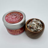 Image of tin of hot chilli seaweed salt with a wooden pot next to it holding chilli seaweed salt