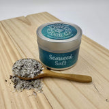 tin of seaweed salt on wooden board with small wooden spoon filled with seaweed salt